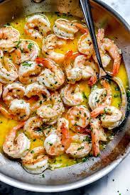 Shrimp cooking in a sauce of butter and wine. It is being stirred with a spoon.